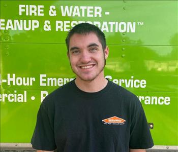 A young man in SERVPRO shirt with short, dark hair standing in front of the rear of a green SERVPRO box truck
